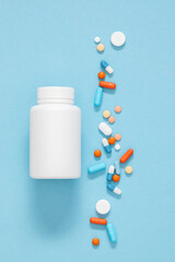 White pill bottle with scattered capsules and tablets on light blue background representing medical and pharmaceutical concepts. Pills of different colors and sizes. Top view. Flat lay.