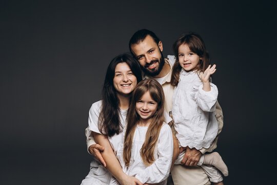 A young sincere family where a stylish bearded father and a cute wife hold their cute children in their arms. Family photo shoot in the studio