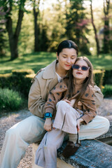 Fototapeta premium hugs of a mother and daughter spending time together on a walk in an aristocratic park, sitting by a fountain