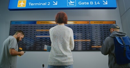 Passengers with Baggage and Tickets Checking Departures on Flight Information Screen. Diverse...