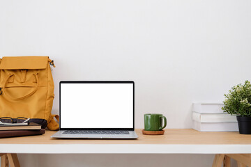 Front view of work desk with yellow bag leaning against wall and laptop with blank screen.