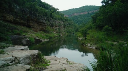 Fototapeta premium Serene river flowing through lush green hills with rocky banks and tranquil reflections