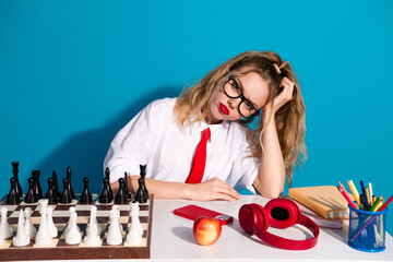 Young woman dressed as a schoolgirl with chess and colorful accessories on desk