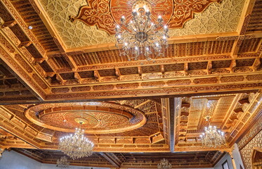 Ornate wooden ceiling with intricate carvings and chandeliers, showcasing Islamic architectural...