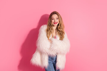 Smiling woman wearing a trendy fur coat standing against a bright pink background, representing...