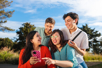 Fototapeta premium Group of young students laughing and using smartphone for taking a selfie in the park