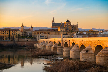 Scenic view of the historic Puente Romano and La Mezquita Cathedral in the background in Cordoba, Andalusia, Spain in golden hour at sunset. Roman Bridge on Guadalquivir river and The Great Mosque.