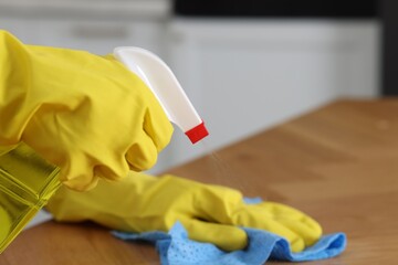 Woman using cleaning product while wiping wooden table with rag indoors, closeup. Space for text