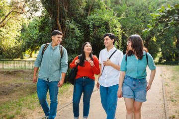 Four happy students with backpacks walking in the park, after class