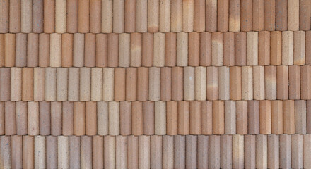 A textured brick wall with cylindrical clay bricks arranged in a horizontal pattern, creating a rustic and earthy surface.