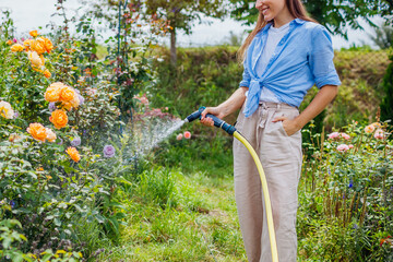 Woman gardener watering plants with hose pipe in summer garden. Taking care of blooming flowers....