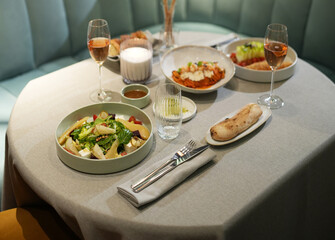 A table set for two with several dishes: a fresh salad, a main course, and a side of bread. The...