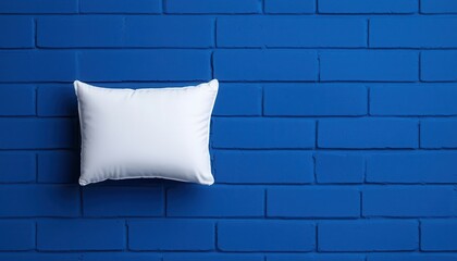 A simple white pillow rests against a vibrant blue brick wall, creating a striking visual contrast for interior decor.