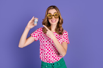 Smiling woman holding rolled dollar bills while showing a golden sunglasses expression against a purple background