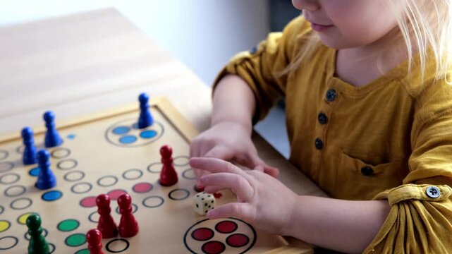 close-up of hands of small child manipulate with wooden figurines of family board game, smart kid, 2-year-old girl is learning to count, Cross and circle game Parcheesi, foreground focus
