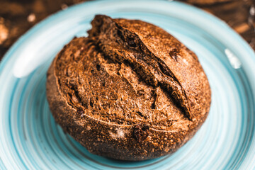 A loaf of rye bread on a turquoise or blue plate on a brown background. Close-up. Top view, Space for text