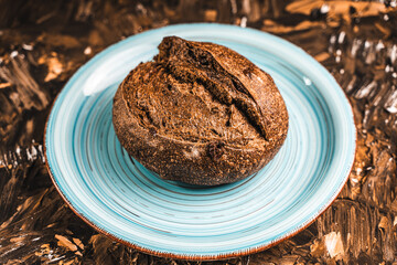 A loaf of rye bread on a turquoise or blue plate on a brown background. Close-up. Top view, Space for text
