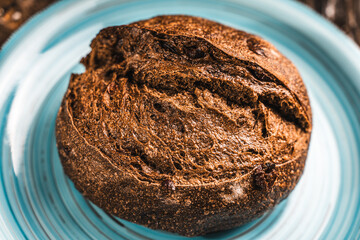 A loaf of rye bread on a turquoise or blue plate on a brown background. Close-up. Top view, Space for text