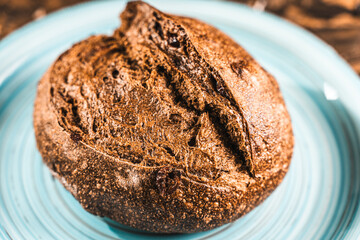 A loaf of rye bread on a turquoise or blue plate on a brown background. Close-up. Top view, Space for text