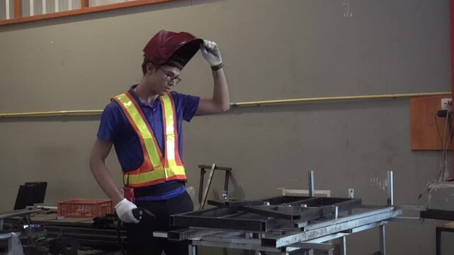 Young Welder at Work: A young male individual in a workshop setting, wearing a welding mask and a high-visibility vest.