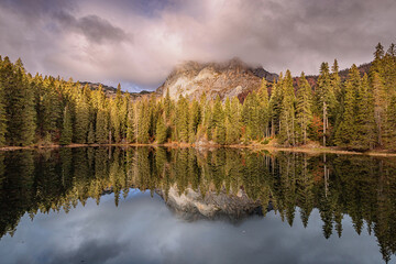 Stunning alpine scenery with crystal clear lake reflecting majestic mountain peaks and colorful autumn forest