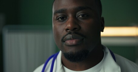 Obraz premium In a hospital setting, a young African physician poses with a warm smile, stethoscope draped around his neck, and dressed in a white coat.