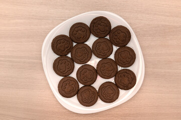 Black cookies with white icing filling lie on a white plate.