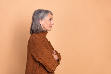 Side profile of an elderly woman wearing a brown sweater against a beige backdrop demonstrating...
