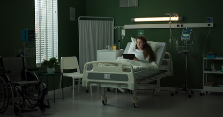 Patient in a hospital room uses a tablet while lying in bed.