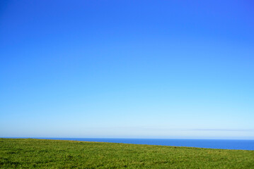 Horizonte marino asomando tras ladera verde y cielo azul