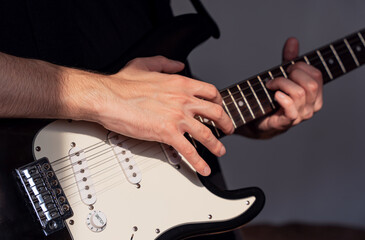 Close-up of the middle part of a man playing an electric guitar, right hand in focus above the...