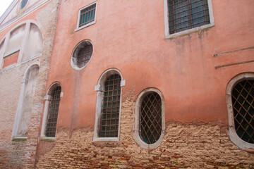Facade of an old Italian brick house with square and rounded windows with lattice in Venice, Italy