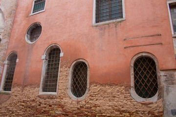 Facade of an old Italian brick house with square and rounded windows with lattice in Venice, Italy