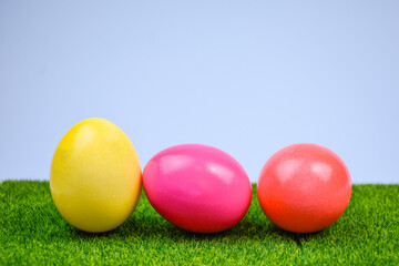Three brightly colored Easter eggs - yellow, pink and red - are placed on green grass against a blue sky. Spring theme, Easter symbols and festive mood.