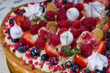 Elegant heart-shaped cake with fresh berries, cream, and meringue.