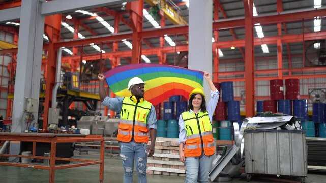 Diversity and Inclusion in Industry: Two construction workers, a man and a woman, stand proudly in a factory holding a rainbow flag, symbolizing diversity and inclusivity in the industrial sector.