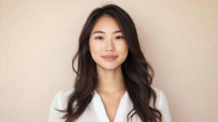 Obraz premium Portrait of an Asian woman with clear skin and natural smile on a soft beige background, representing beauty and skincare concepts in a studio setting.