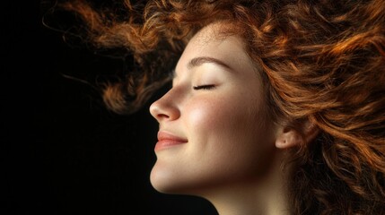 Fototapeta premium Curly-haired woman smiling with closed eyes as she turns her head, showcasing vibrant red curls against a minimalist black background.