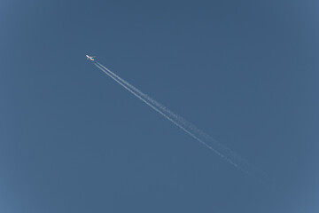 A high-flying airplane leaves a contrail across a clear, azure sky, showcasing the beauty of flight and the vastness of the atmosphere