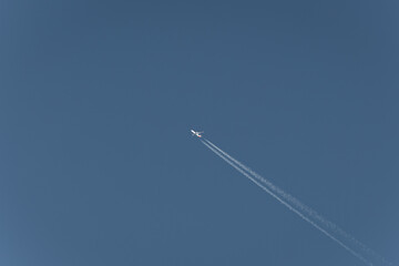 A high-flying airplane leaves a contrail across a clear, azure sky, showcasing the beauty of flight and the vastness of the atmosphere