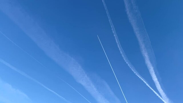 the plane flies against the background of the blue sky, leaving an inversion white trail, many traces of chemtrail