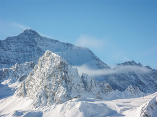 A snowy rocky mountain range and blue sky with a forest near a ski resort in the French or Swiss Alps in the winter