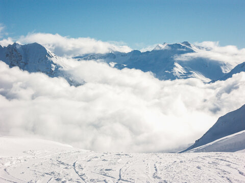 The view from a ski piste of low clouds leaving only the peaks of the snowy mountain tops visible in the winter on a sunny cold day with a clear blue sky