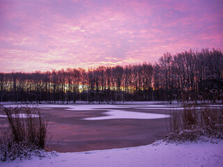The sun coming up on a cold winter morning creating amazing colors and clouds in the purple sky overlooking a frozen lake.