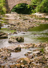 A small river or stream running through the Yorkshire Dales in England with a small bridge in the background