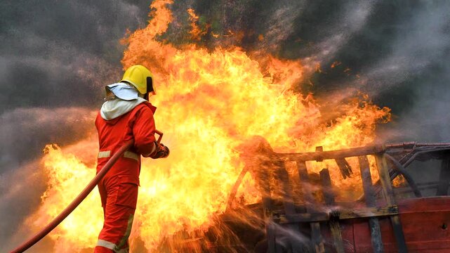 Professional Fireman in fire protection suit fighting strong fire in danger situation. Firefighter teamwork spray water from fire hose to extinguishing fire flames in training operation.