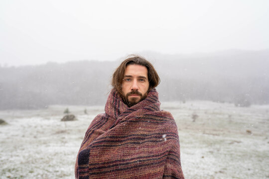 Close up portrait of bearded man wrapped in blanket standing in snowfall outdoors
