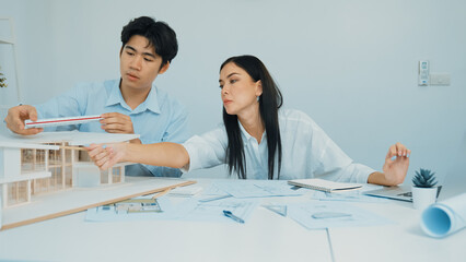 Professional male engineer measure house model by using ruler while beautiful cooperative coworker...