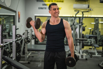 young muscular man do biceps workouts with dumbbells in gym
