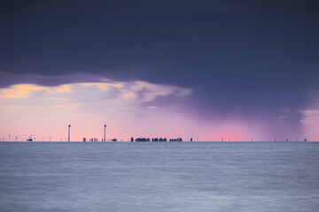 Fototapeta premium Cloudy sunset with sunbeams above the water surface of the IJsselmeer with the Amsterdam skyline on the horizon
